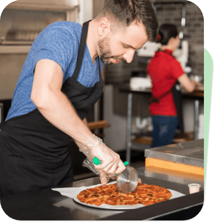 Restaurant worker preparing a pizza in a busy kitchen.